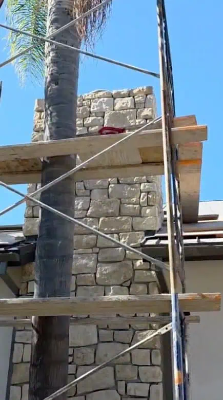 Skilled stone masonry wall construction with scaffolding and palm tree.